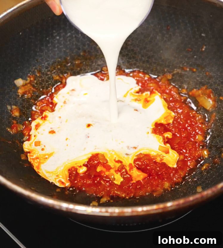 Creamy Gochujang Pasta Recipe 5 A stream of heavy cream being poured into a sizzling pan of gochujang sauce and caramelized onions, forming the rich base for the creamy gochujang pasta.