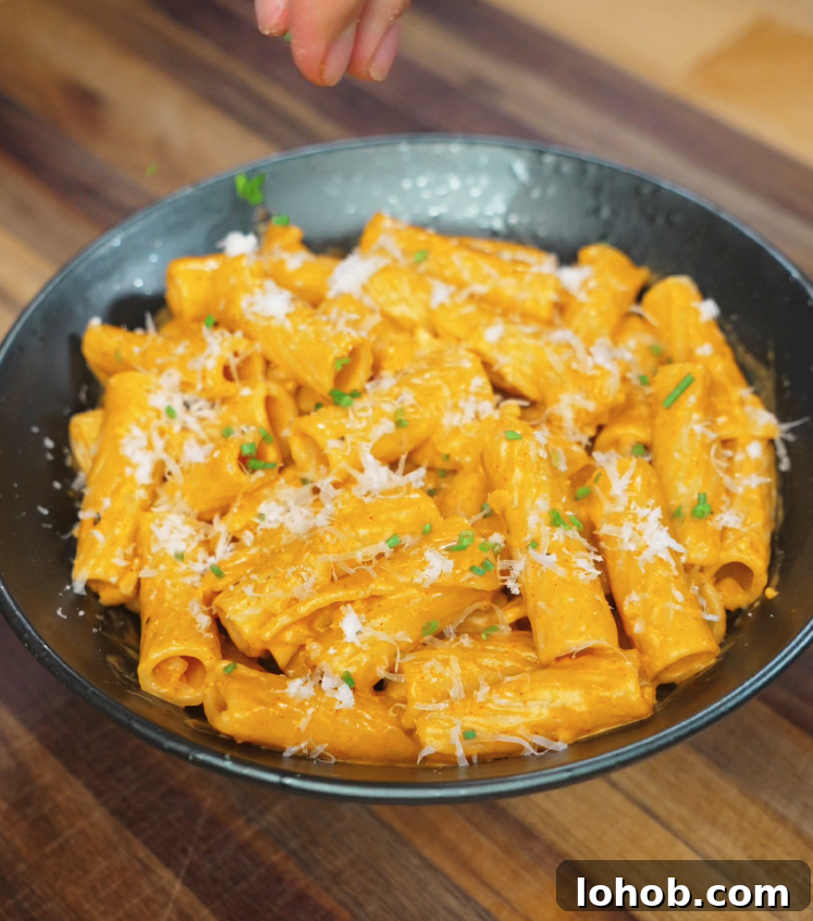 Creamy Gochujang Pasta Recipe 7 A hand sprinkling freshly grated parmesan and chopped chives over a bowl of creamy gochujang pasta for a final touch of flavor and color.