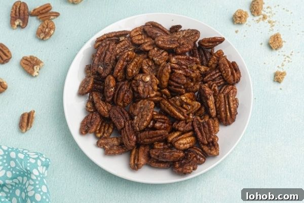 Crispy Spiced Pecans Made in the Air Fryer 2 Spiced Pecans served on a white plate with scattered pecans and brown sugar on the table.