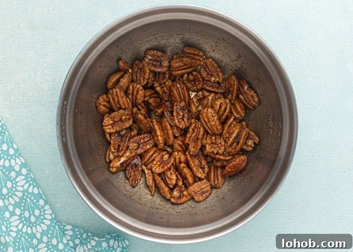 Crispy Spiced Pecans Made in the Air Fryer 3 Pecans in a metal mixing bowl, sitting in the soy sauce and seasonings before being cooked in the air fryer.