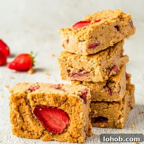 Gooey Chickpea Blondies with Chocolate Chips 3 Four chickpea blondies with strawberries stacked on top of each other, there is another one on its side in front. There are some strawberries in the background.