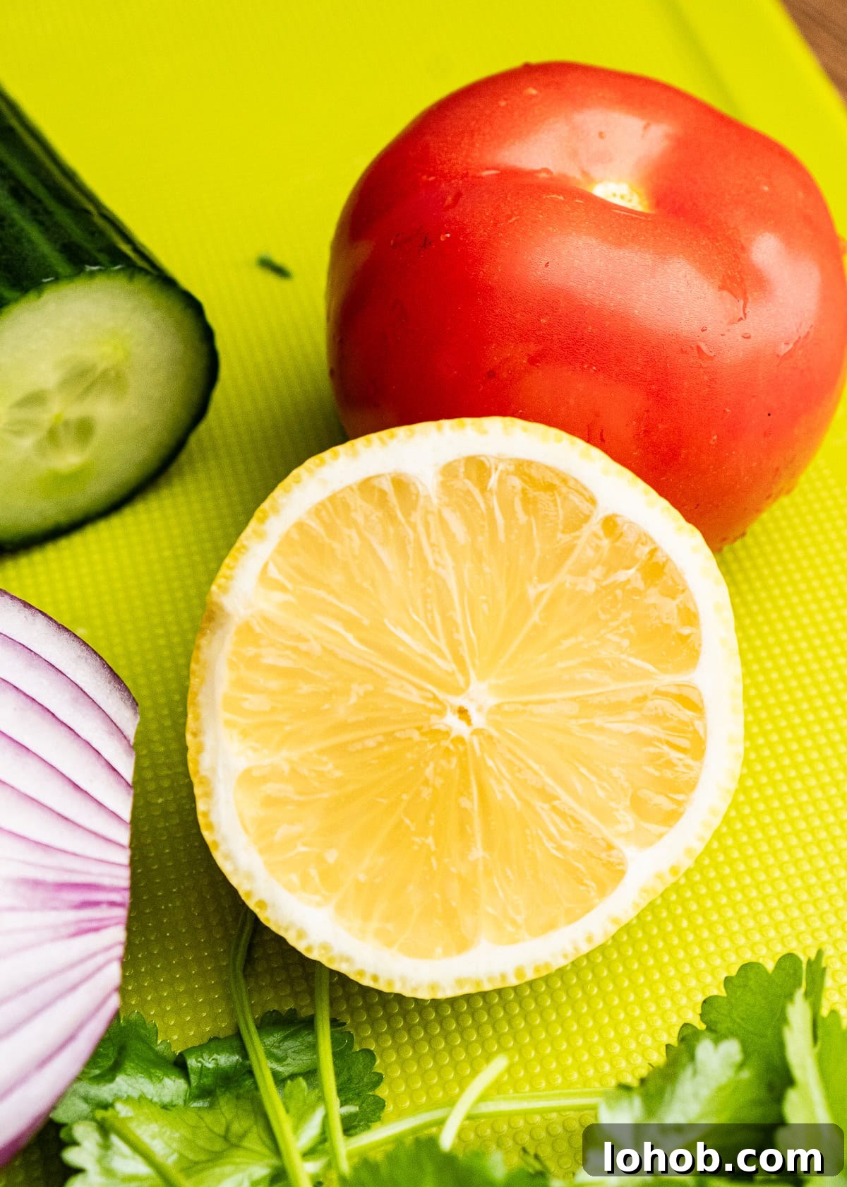 Kachumber: Tangy Indian Onion Salad 9 A cut half a lemon on a green chopping board with a tomato in the background