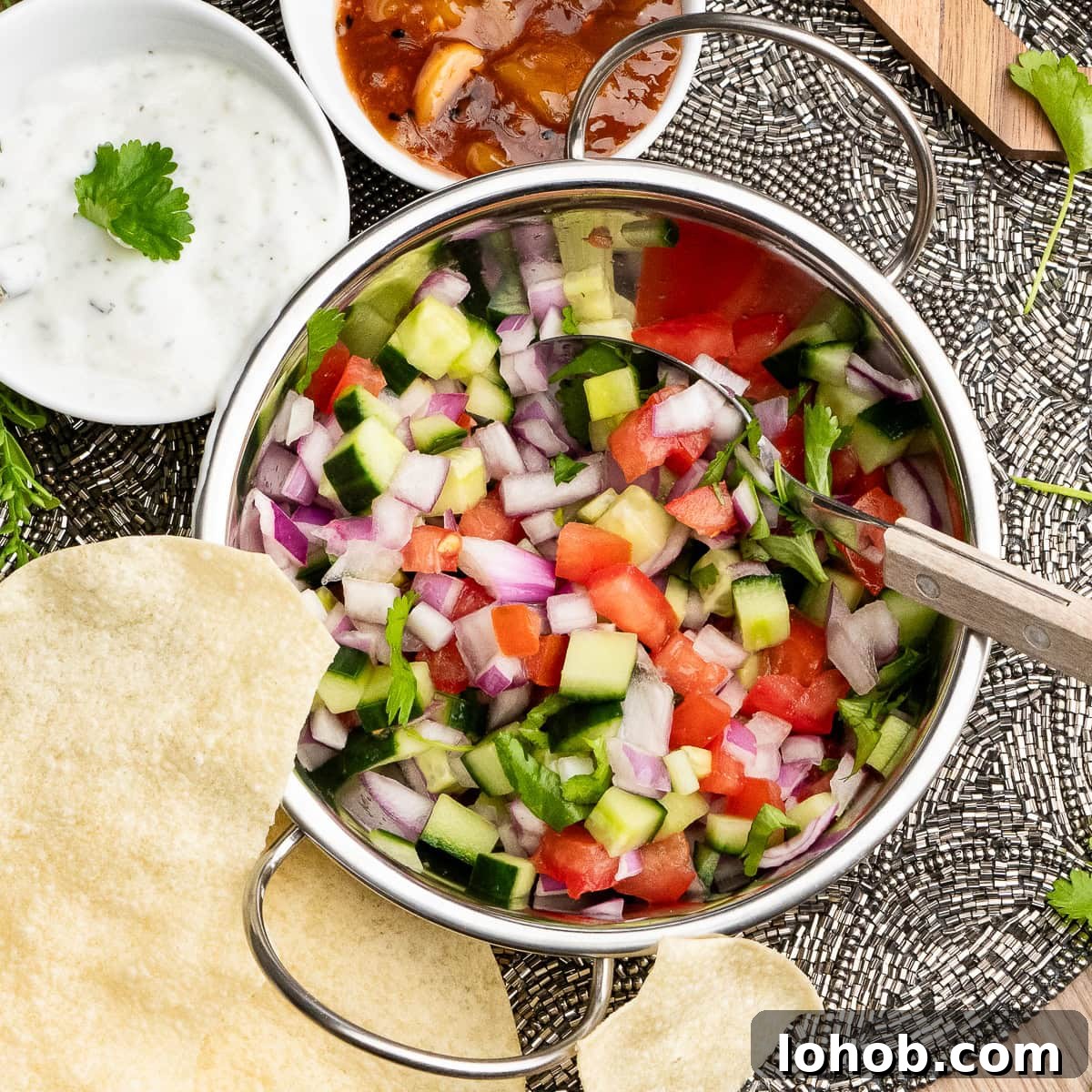 Kachumber: Tangy Indian Onion Salad 11 Indian Onion Salad with a spoon on top of the salad in a Balti dish with, mint raita, mango chutney and poppadoms served on the side.
