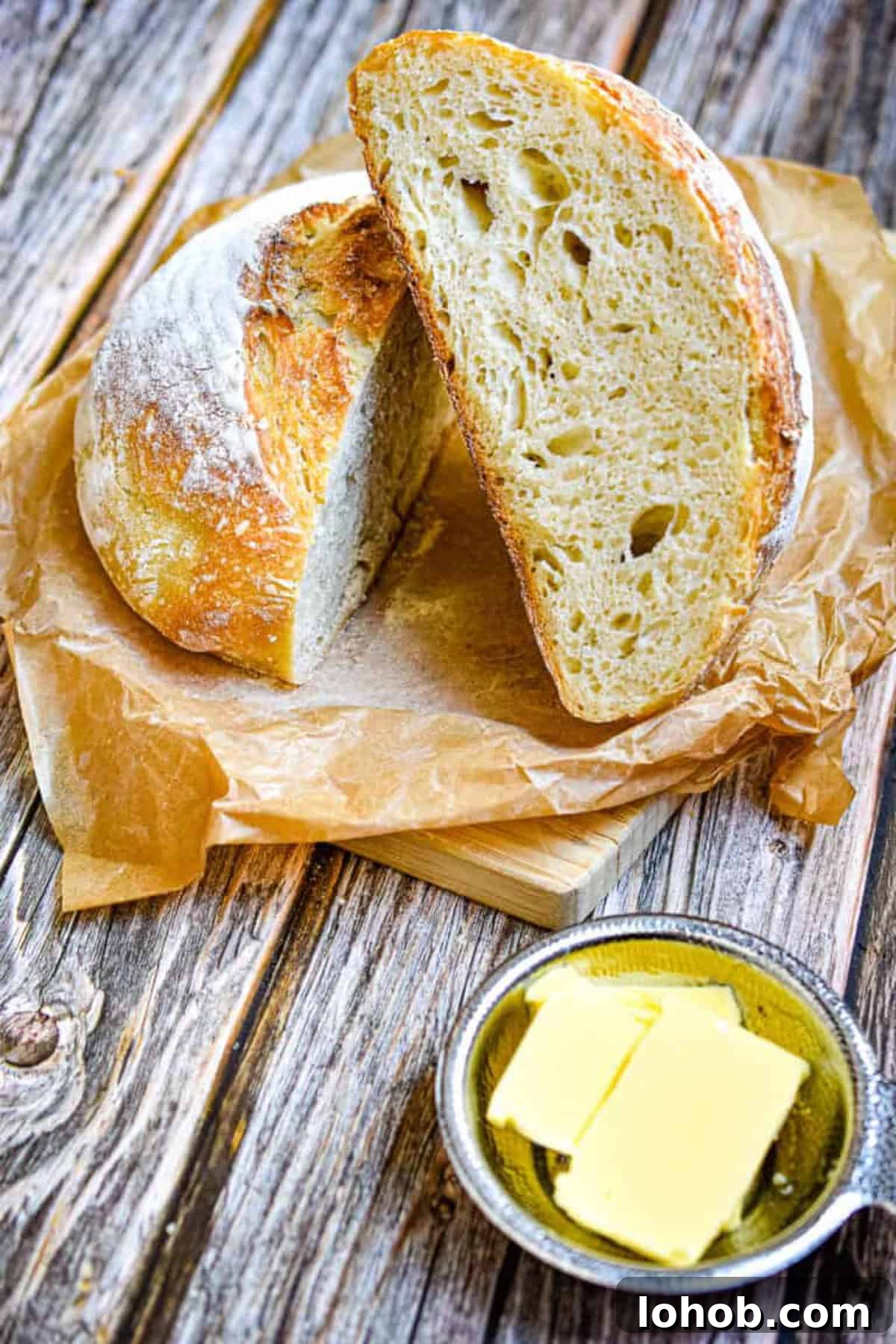 Sourdough Hydration: Mastering Dough Water Ratios 5 Two halves of loaves are on a piece of parchment paper with a bowl of butter in front.