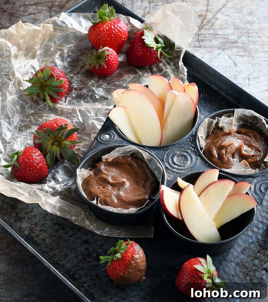 Chocolate hummus and date caramel hummus in an antique muffin tin with apples slices and strawberries.
